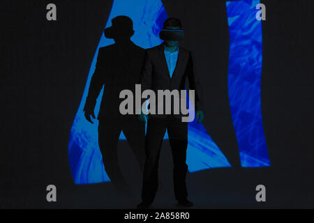 Dark double exposure businessman with virtual reality simulator glasses against AI text Stock Photo