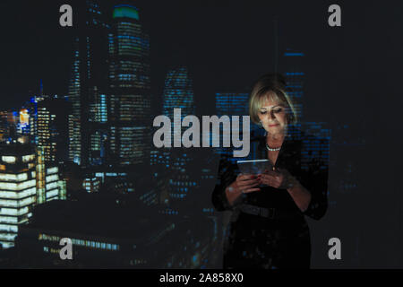 Double exposure businesswoman using digital tablet against highrise lights at night Stock Photo