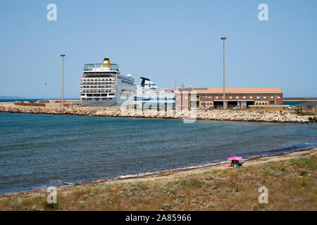 A lone pink beach parasol on a beach in a industrial ferry port urban landscape setting in Porto Torres Sardinia Italy Europe. Stock Photo