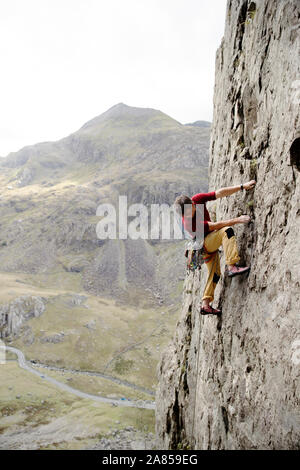 Male rock climber scaling rock face, looking down Stock Photo