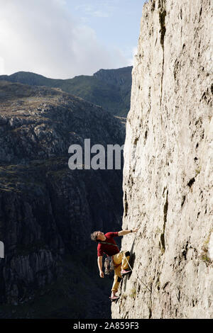 Male rock climber scaling large rock face, looking up Stock Photo