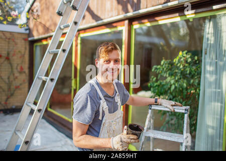 Portrait confident male painter with ladder painting home exterior Stock Photo