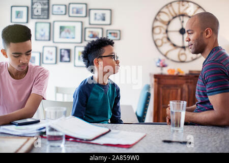 Father and sons talking, doing homework in kitchen Stock Photo
