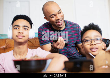 Father and sons eating and watching TV Stock Photo