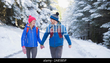 Couple holding hands, hiking on trail in snowy woods Stock Photo