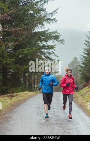 Couple jogging on trail in rainy woods Stock Photo