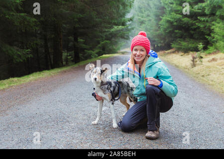 Portrait happy woman with dog hiking on trail in woods Stock Photo