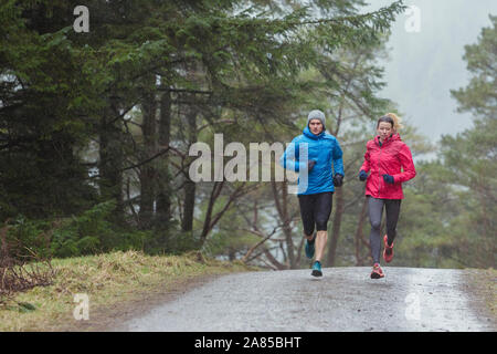 Couple jogging on trail in rainy woods Stock Photo