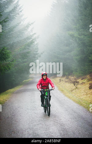 Man mountain biking on trail in rainy woods Stock Photo