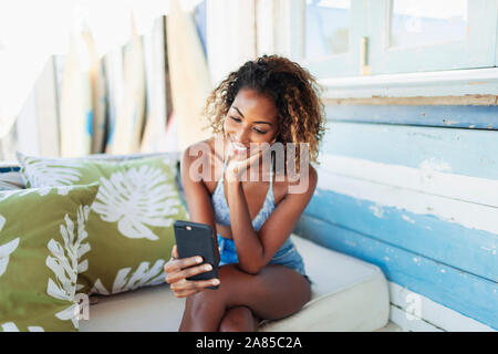 Happy young woman using smart phone on beach hut patio Stock Photo