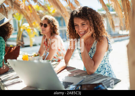 Young woman using laptop at sunny beach bar