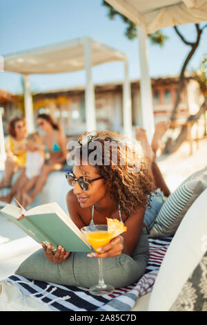 Carefree woman relaxing, reading book and drinking cocktail on beach patio Stock Photo