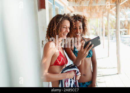 Happy young women friends in bikinis taking selfie on beach hut patio Stock Photo