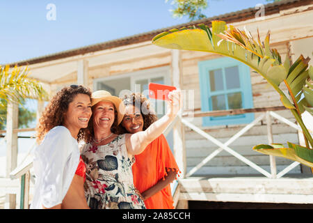 Happy mother and adult daughters taking selfie outside sunny beach hut Stock Photo