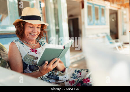 Happy woman reading book on beach hut patio Stock Photo