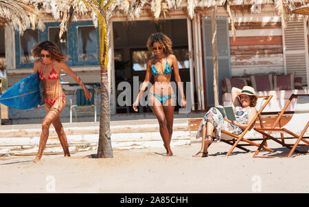 Young women in bikinis with surfboard on sunny beach Stock Photo