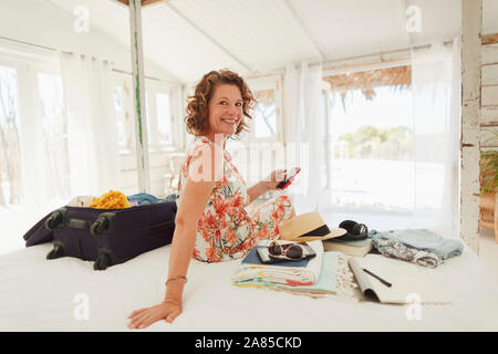 Portrait happy woman unpacking suitcase on beach house bed Stock Photo