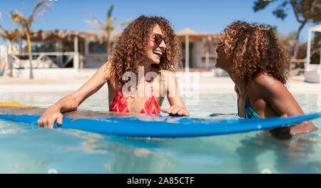 Happy sisters with surfboard in sunny ocean Stock Photo