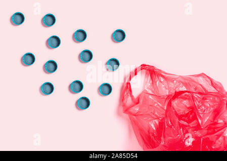 Plastic red bag surrounded by plastic bottle cups on pink background. Flat lay, top view, copy space. Stock Photo