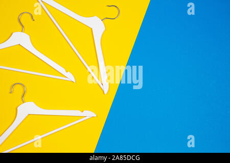 White wooden clothes hangers on yellow and light blue background. Top view. Shopping, sale, promo, new season concept Stock Photo