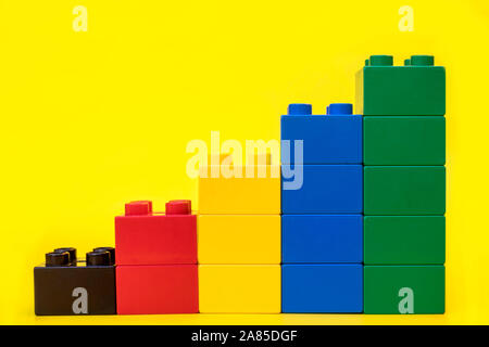 Bar graphs plastic building blocks toy bricks on yellow background. Stock Photo