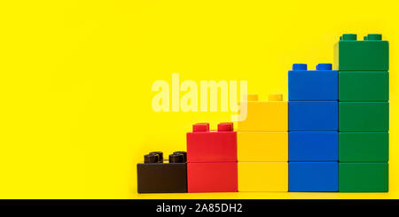 Bar graphs plastic building blocks toy bricks on yellow background with place for you text and content. Stock Photo
