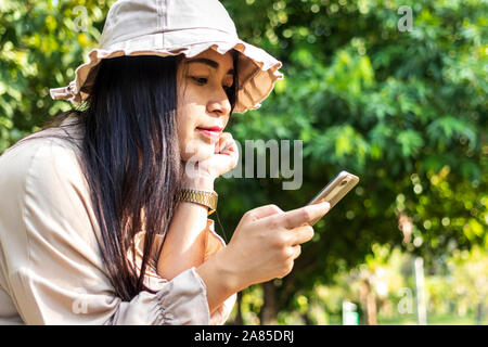 Young happy woman using smartphone. Beautiful smiling woman use of mobile phone in public park. Stock Photo