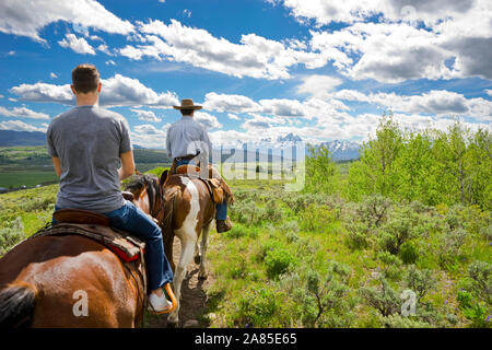 Two men ride horses with the Teton mountain range in the distance Stock Photo