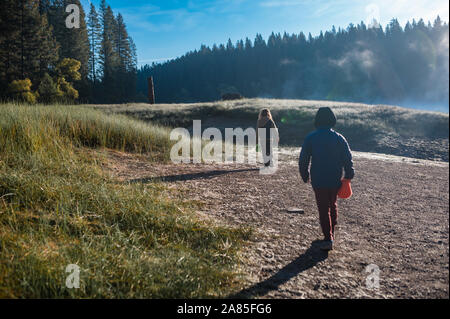 Two children walking in a meadow near a foggy lake at Sly Park Stock Photo