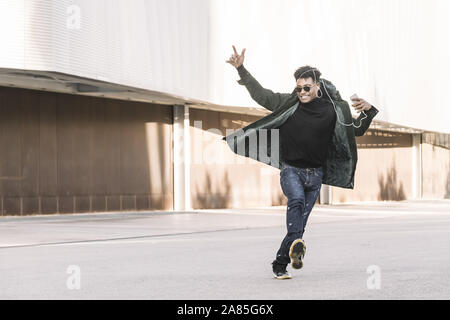 black young man with earphones dancing happy by the city and listening music with a mobile phone, technology and lifestyle concept using internet elec Stock Photo