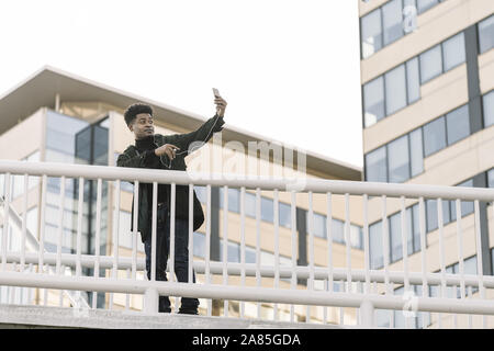 happy black man posing for selfie on smartphone camera while listen music in headphones or making video call outdoors in the city, technology and life Stock Photo