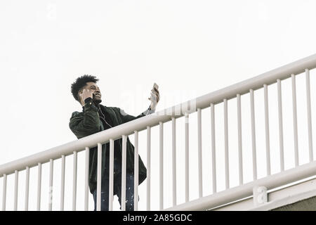smiling black man with smartphone listening music in earphones or making video call outdoors in the city, technology and lifestyle concept using inter Stock Photo