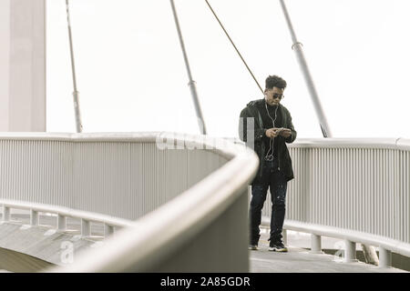 black man walks around looking at his smartphone while listen music in earphones in the city, technology and lifestyle concept using internet electron Stock Photo