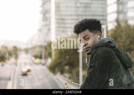 attractive young black african man with green jacket listening music with white earphones in the city, lifestyle concept Stock Photo