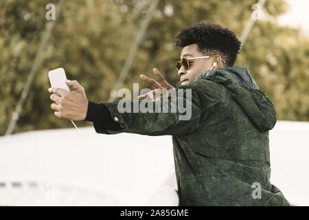 cool young african black man taking a selfie with smartphone and earphones while poses for the photo, city lifestyle and technology concept using inte Stock Photo