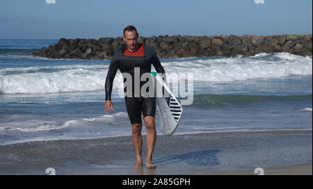 Paddle boarder (athletic man in his early 50's) carrying his board out of the ocean after a morning of exercise