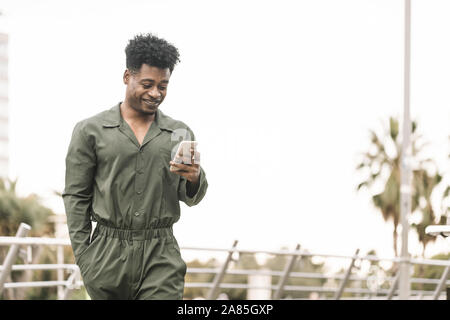 handsome young african black man smiling and texting message on smartphone while walks in a park outdoors in the city, lifestyle and technology concep Stock Photo