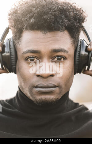 vertical portrait of a serious african black man listening music with the hands touching the headphones, technology and lifestyle concept Stock Photo