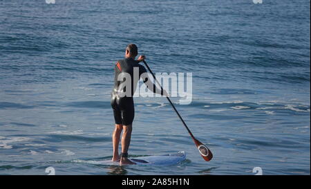 Athletic man (52 year old Caucasian) paddles flat ocean water on a SUP (stand up paddle board) Stock Photo