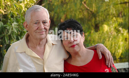 Happy, older couple smiling. The man (80 year old Caucasian) has his arm around his wife's shoulder (62 year old Hispanic). Stock Photo
