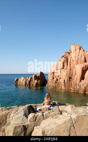 Sunbathing at the Rocce rosse / Porphyry Red Rocks Beach Arbatax, Ogliastra coast in Tortolì, Sardinia, in Italy - sunbather Stock Photo