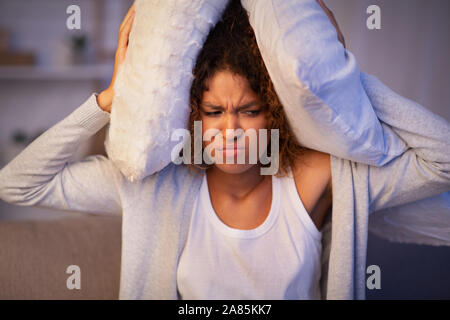 Irritated girl covering ears with pillows because of noise Stock Photo