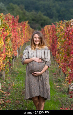 Pregnant woman between a row of grape vines in autumn Stock Photo