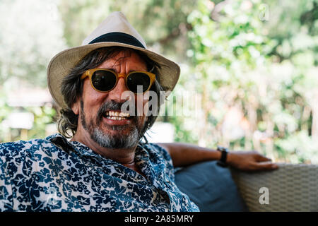 Stock photo of a man with a hat and sunglasses smiling at camera leaning on a sofa Stock Photo