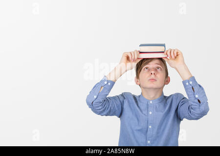 Stressed teenager holding books on his head having exams and feeling overwhelmed, depressed and exhausted . Concept of education. Stock Photo