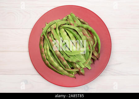 Fresh green flat beans in plate on wooden white table. Top view Stock Photo