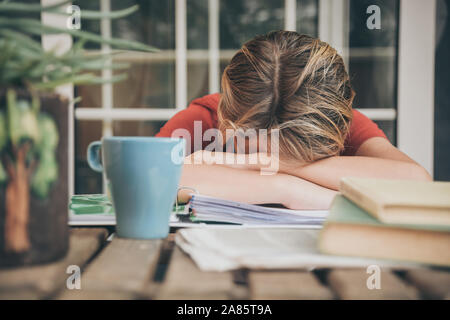 Tired student doing homework at home sitting outdoor with school books and newspaper. Boy weary due to heavy study. Kid asleep on the copybook Stock Photo