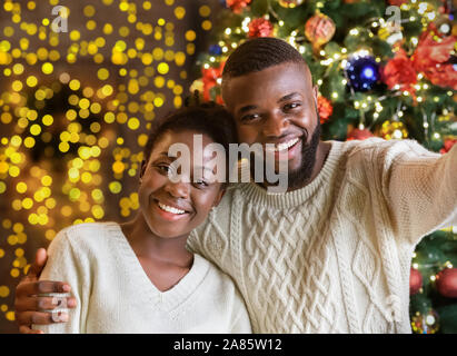 Happy black couple making selfie with Christmas tree on background Stock Photo