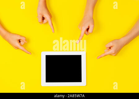 Many kids hands pointing to tablet computer on yellow background Stock Photo