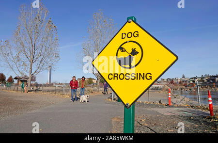A sign marks a dog crossing area on a walking path along the Deschutes River in Bend, Oregon Stock Photo